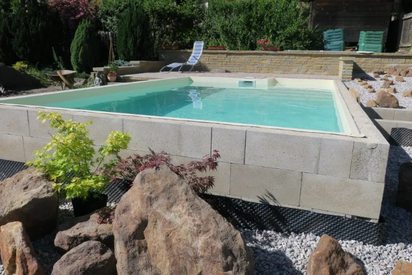 Záběr na bazén z pohledu zahrady - skalka a v pozadí pohled na bazén v nové fólii ALBAblue v pískované barvě