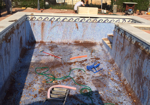 Bazén ve špatném stavu, před rekonstrukci, obélníkový šedý bez potažení, na dně je nepořádek a červené skvrny.