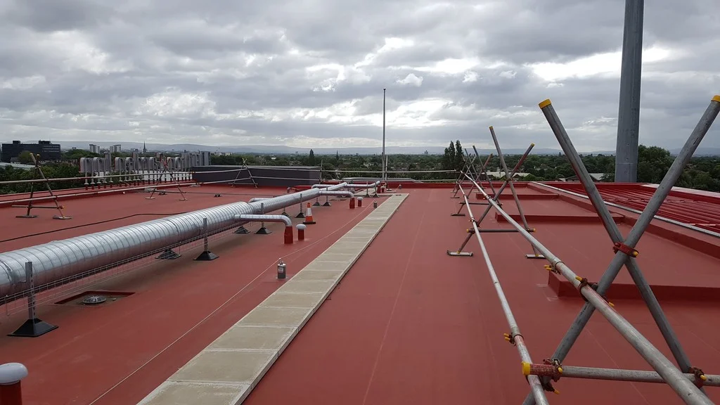 Pohled na červenou střechu hotelu Hilton Garden Inn s fólií Protan SE, ventilačními potrubními rozvody a bezpečnostními zábranami na stadionu Old Trafford.