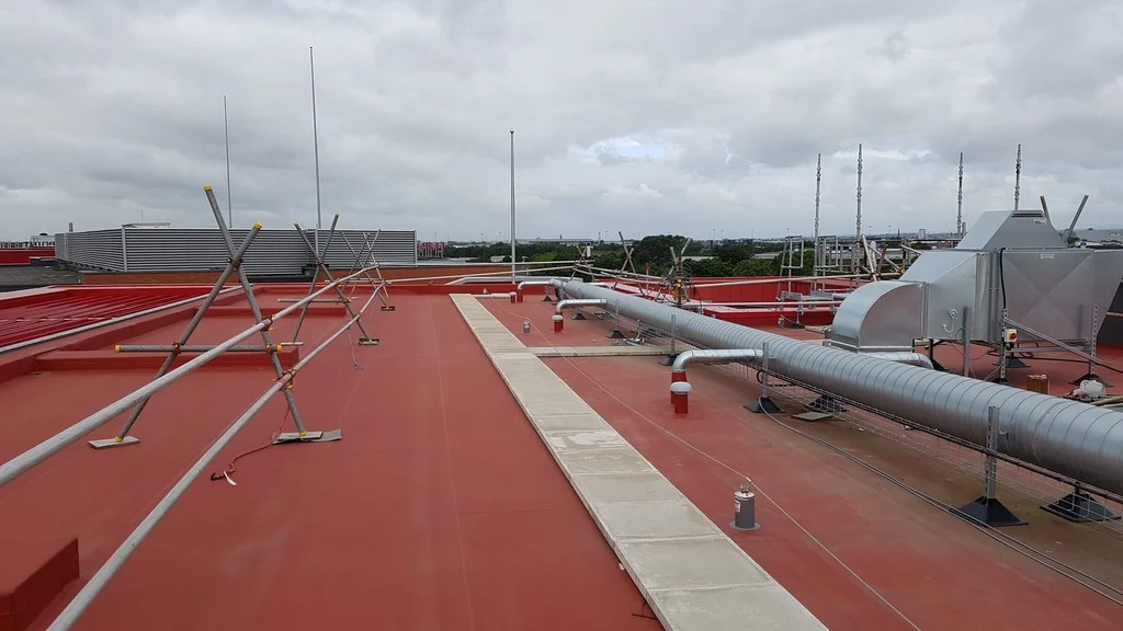 Červená střecha hotelu Hilton Garden Inn na stadionu Old Trafford Cricket Ground s fólií Protan SE, ventilačními potrubími a bezpečnostními zábranami pod zataženou oblohou.