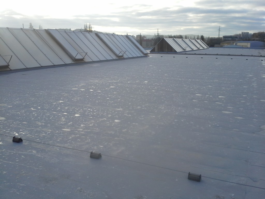 Detail dokončené rovné střechy s hydroizolační fólií Protan SE 1,5 mm, pohled směrem k okolní průmyslové a venkovské krajině.