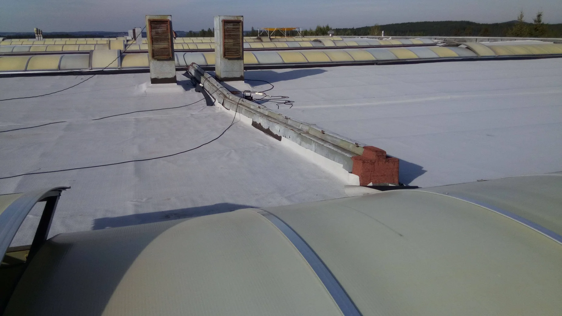 Detail nově položené hydroizolační fólie Protan SE 1,5 mm na střeše výrobní haly Jihostroj ve Velešíně, s napojením kolem střešních prostupů a světlíků.